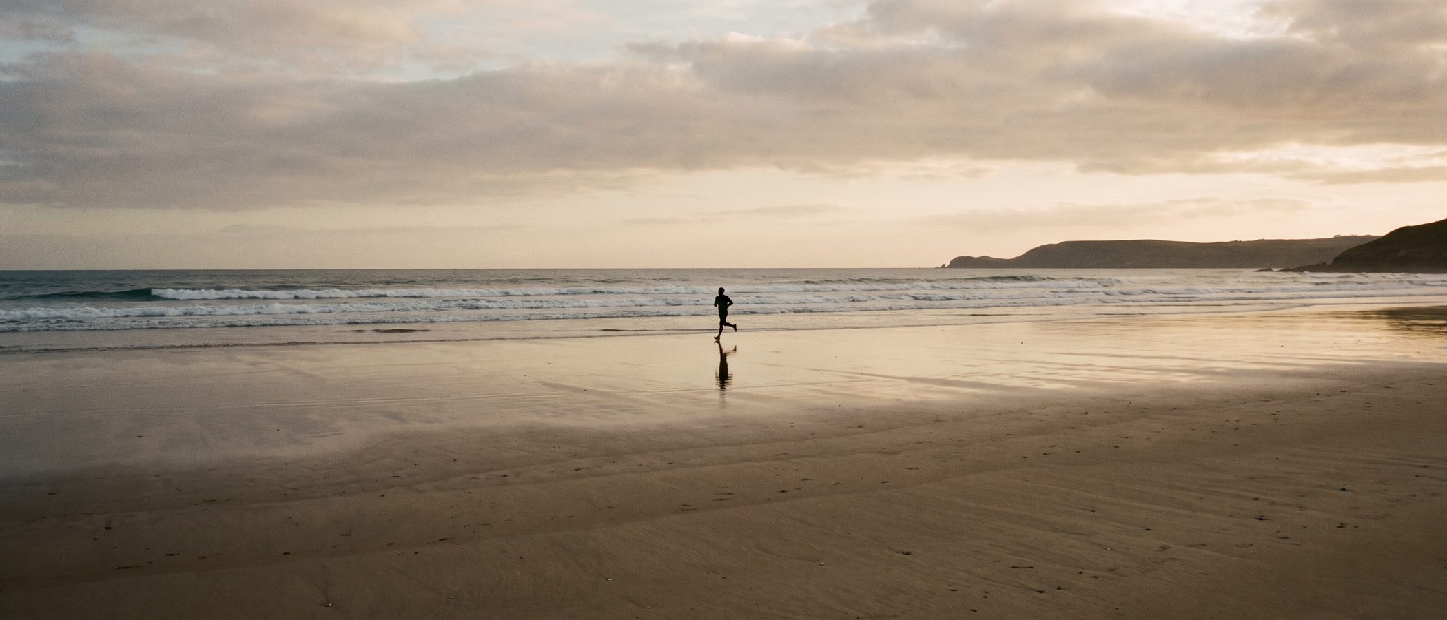 A runner on a wide beach at golden hour